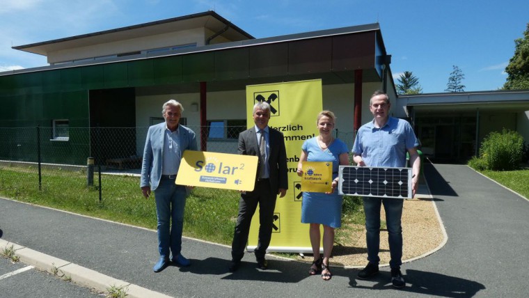 Vier Personen stehen vor einem Kindergarten und halten ein Solar2 Schild und 1 PV-Modul.
